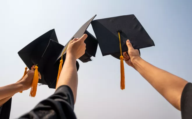 Trois étudiants diplômés tenant leur chapeau de fin d'études.
